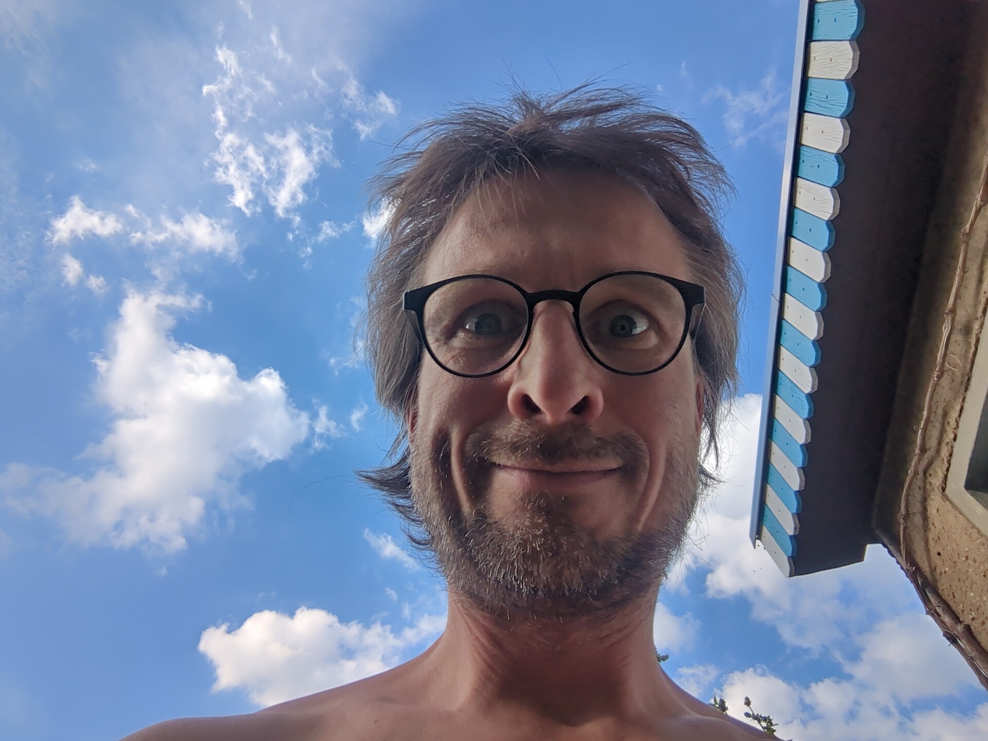 A portrait of the artist framed by books and a bright, cloudy sky.