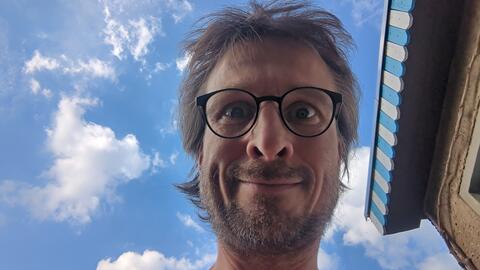 A portrait of the artist framed by books and a bright, cloudy sky.