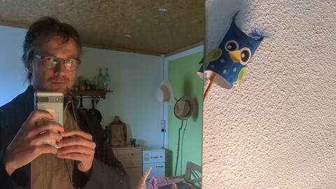 Portrait of the artist alongside a whimsical, handmade wall decoration.