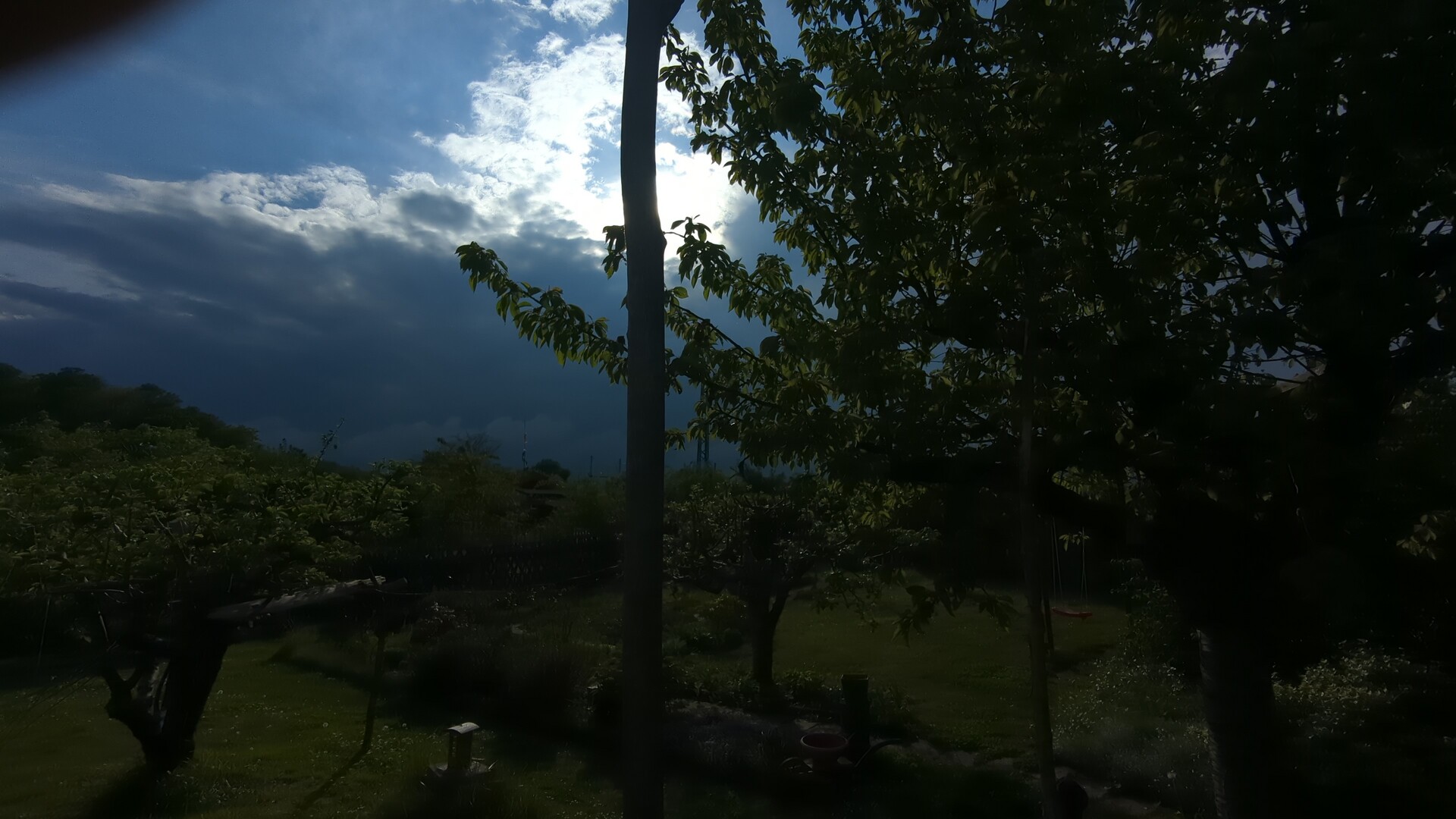 Dramatic sunlight breaks through heavy storm clouds over a lush garden landscape.