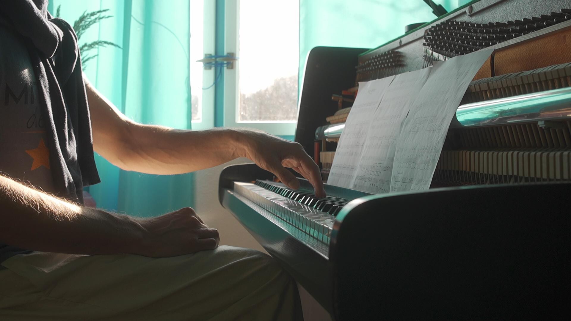 Sunlight illuminates sheet music and hands poised over the keys of a piano.